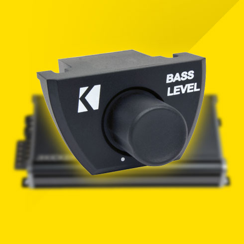 KICKER bass level remote knob in focus with blurred amplifier in background.